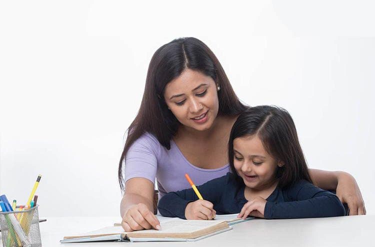 A home tutor smiling as she helps a young girl write in her notebook